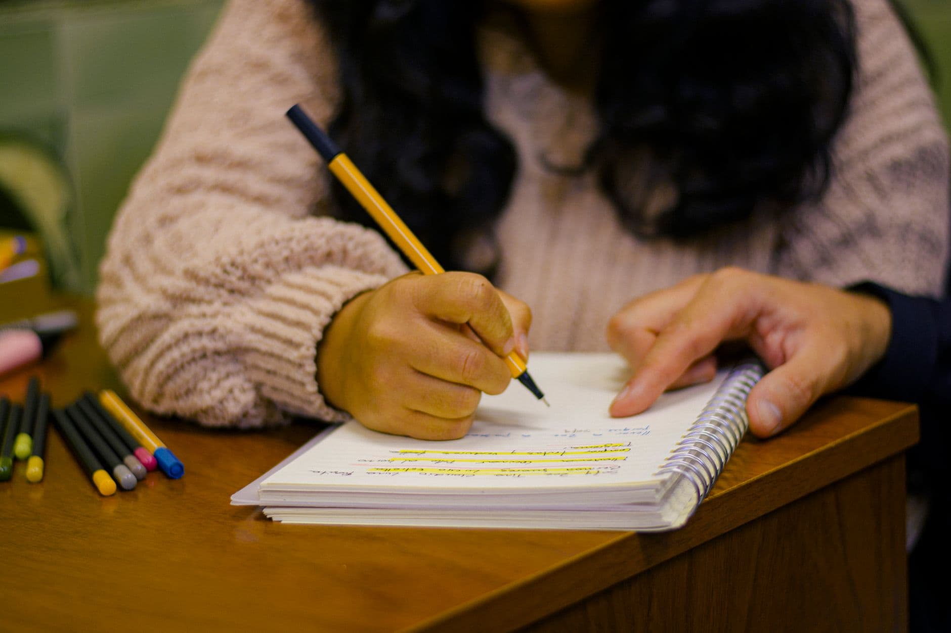 Estudante grifando anotações no caderno sobre a mesa de estudo